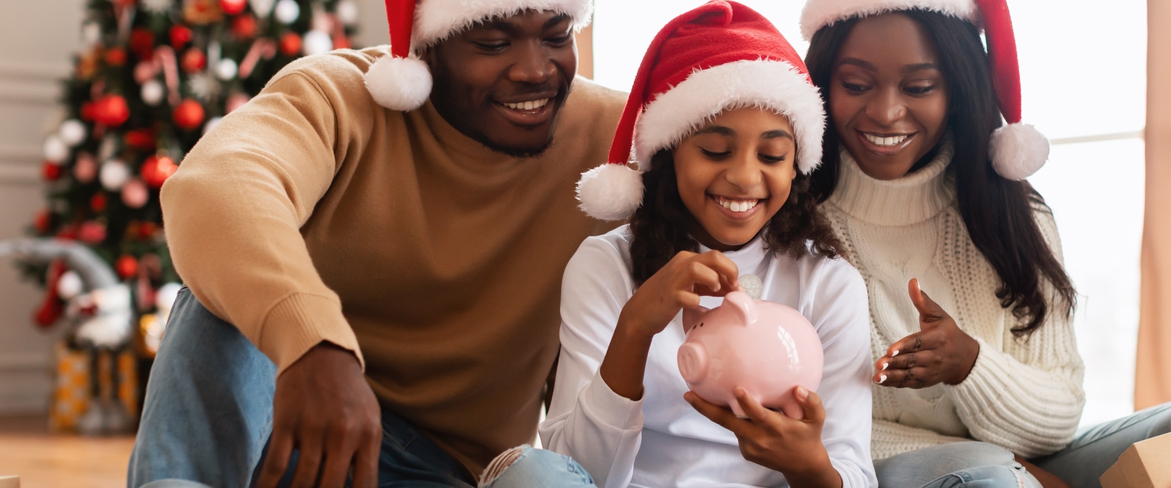 Family with Santa hats. Daughter puts money in a piggy bank.