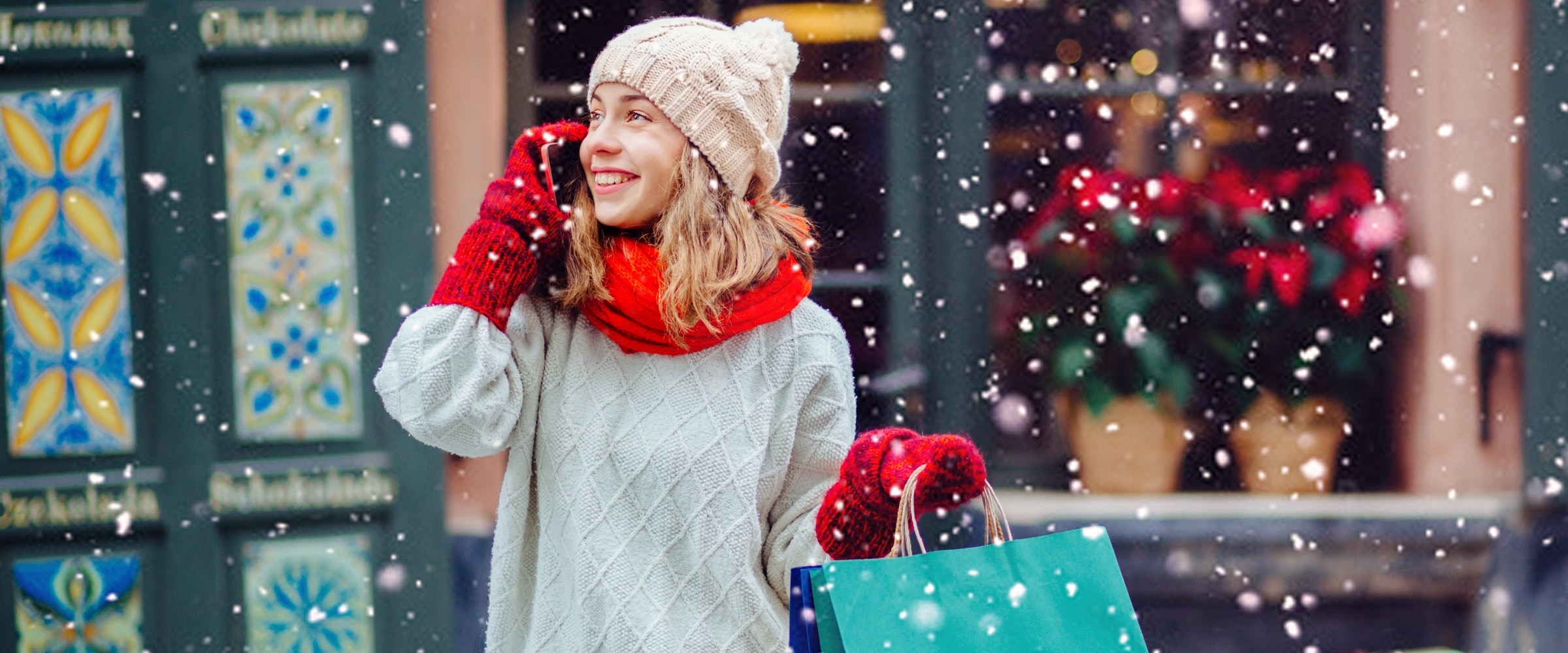 Young woman stands outside store in the snow holding shopping bag.