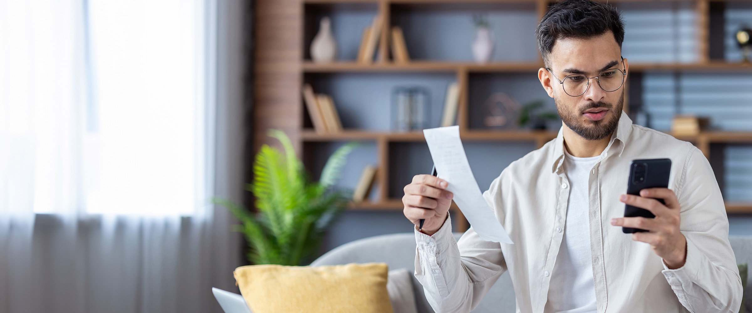 Photo of person looking at data on his smartphone while holding up a store receiptl