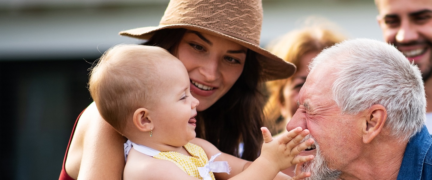 Close of mom holding small child. Older person is smiling at the child.