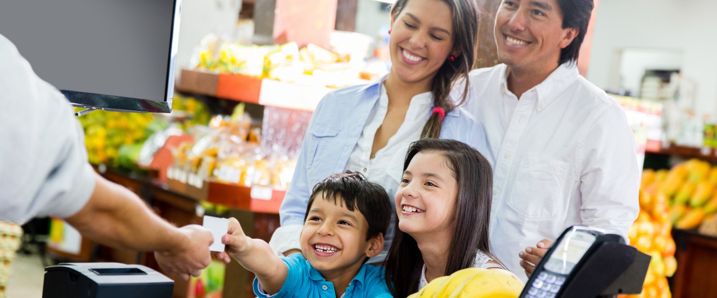 Photo of family at store. One of their younger kids hands credit card to cashier.