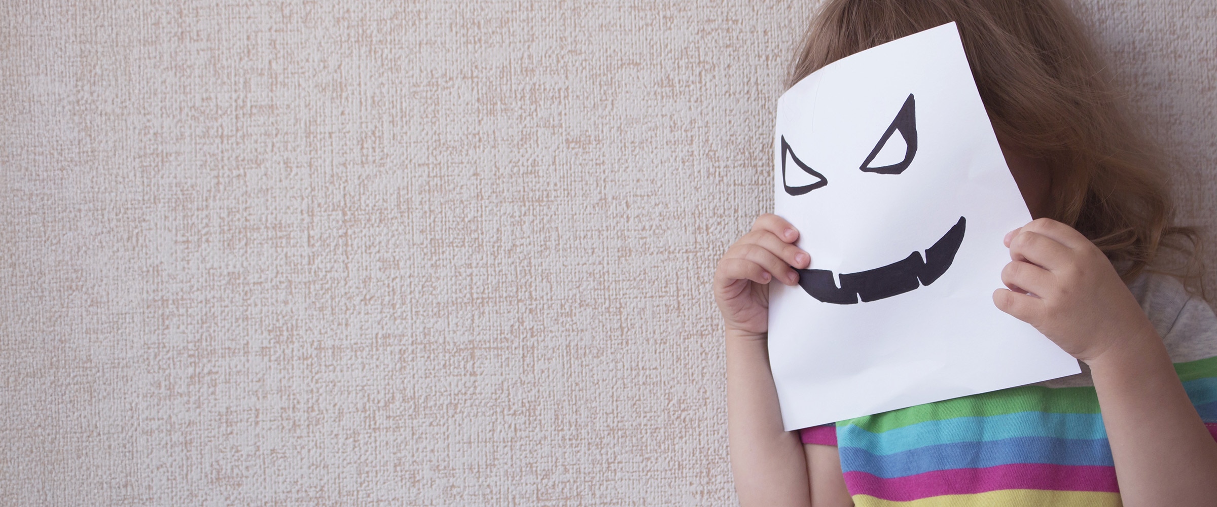 Photo of a child holding up a paper mask over their face.