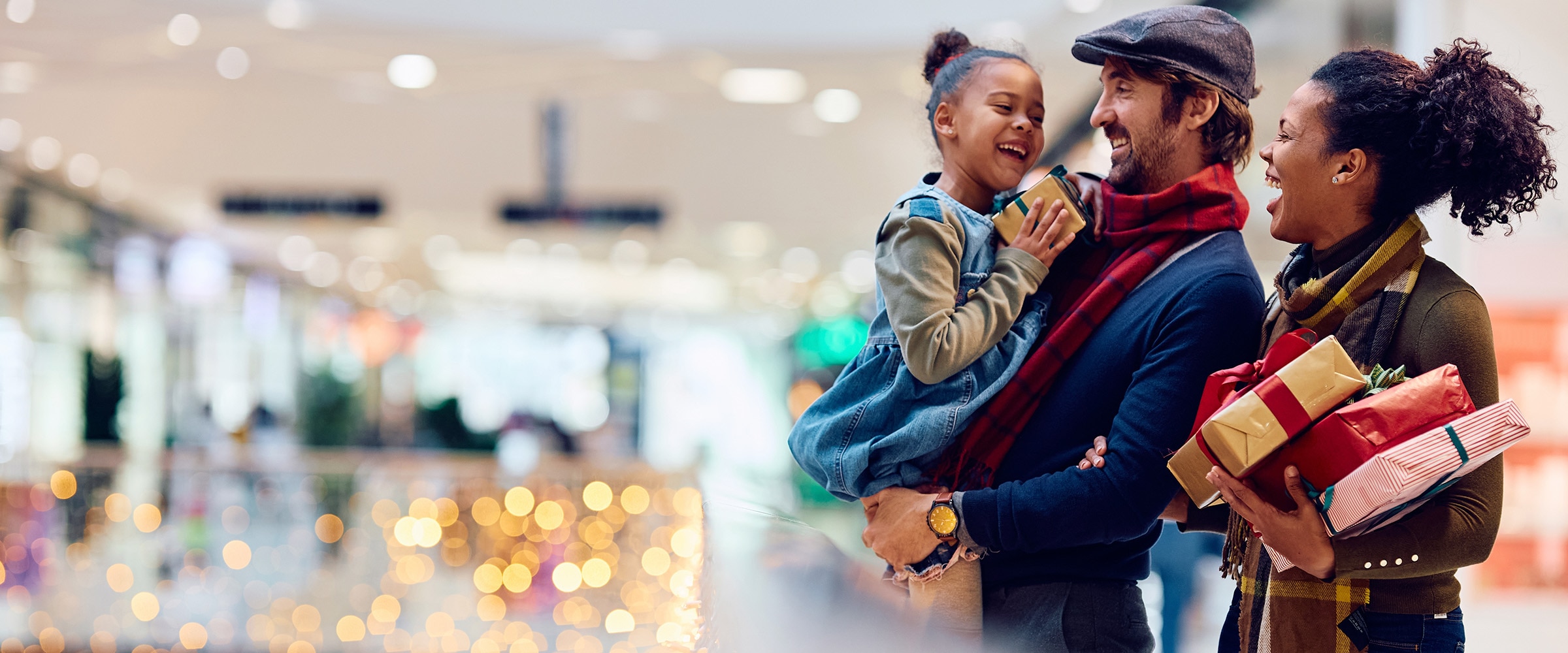 A family at the mall shopping. Their child is in the dad's arms.