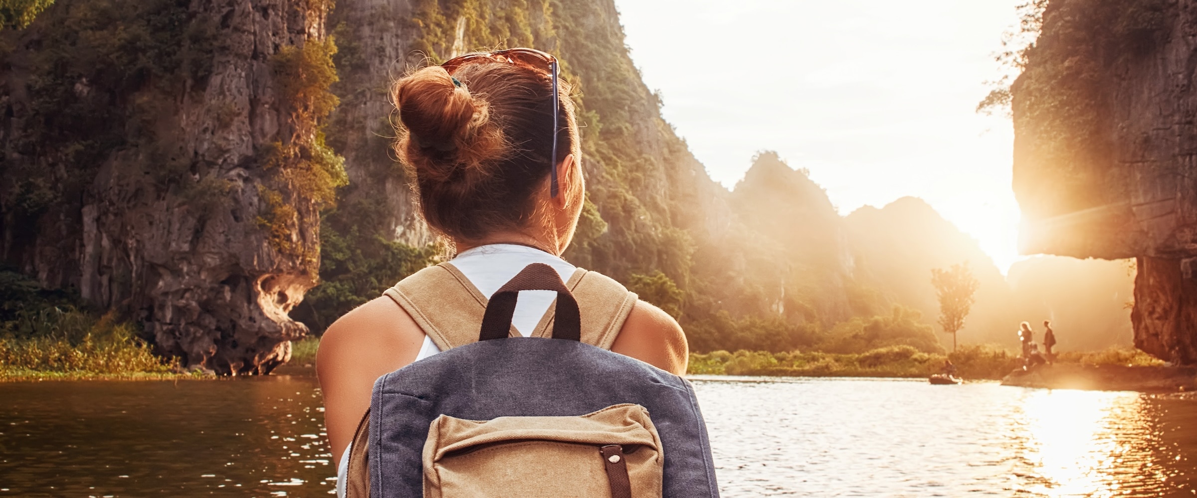 Photo of woman with a backpack on a river facing the sun.