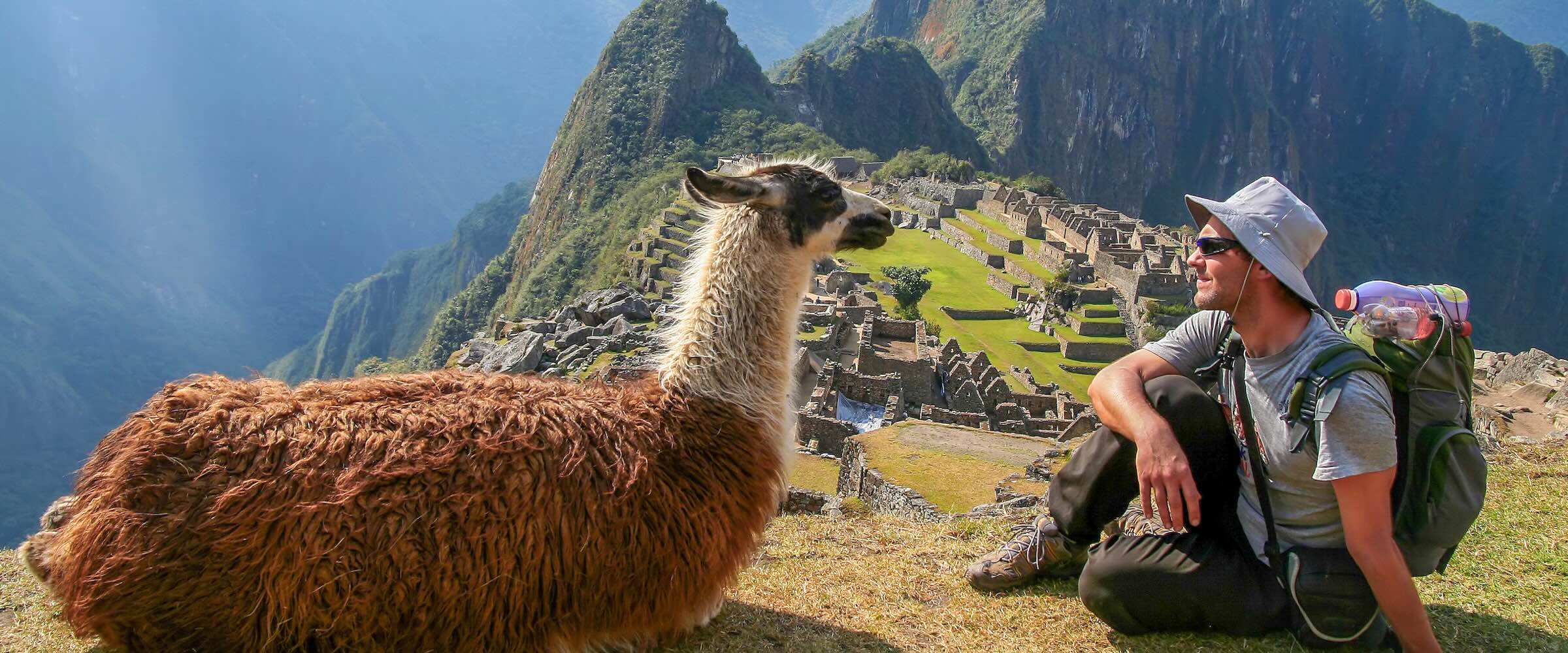 Photo of young traveler sitting next to llama in Machu Picchu.