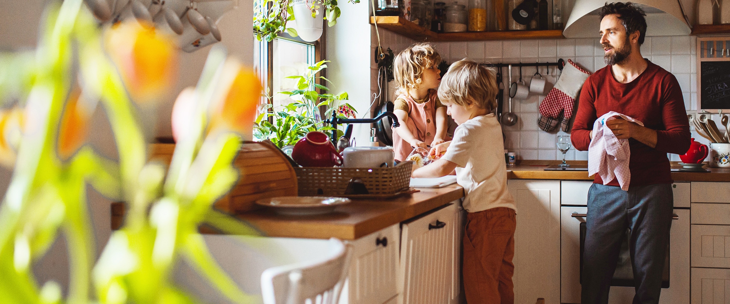 Photo of dad and children in kitchen. Dad is drying dishes.