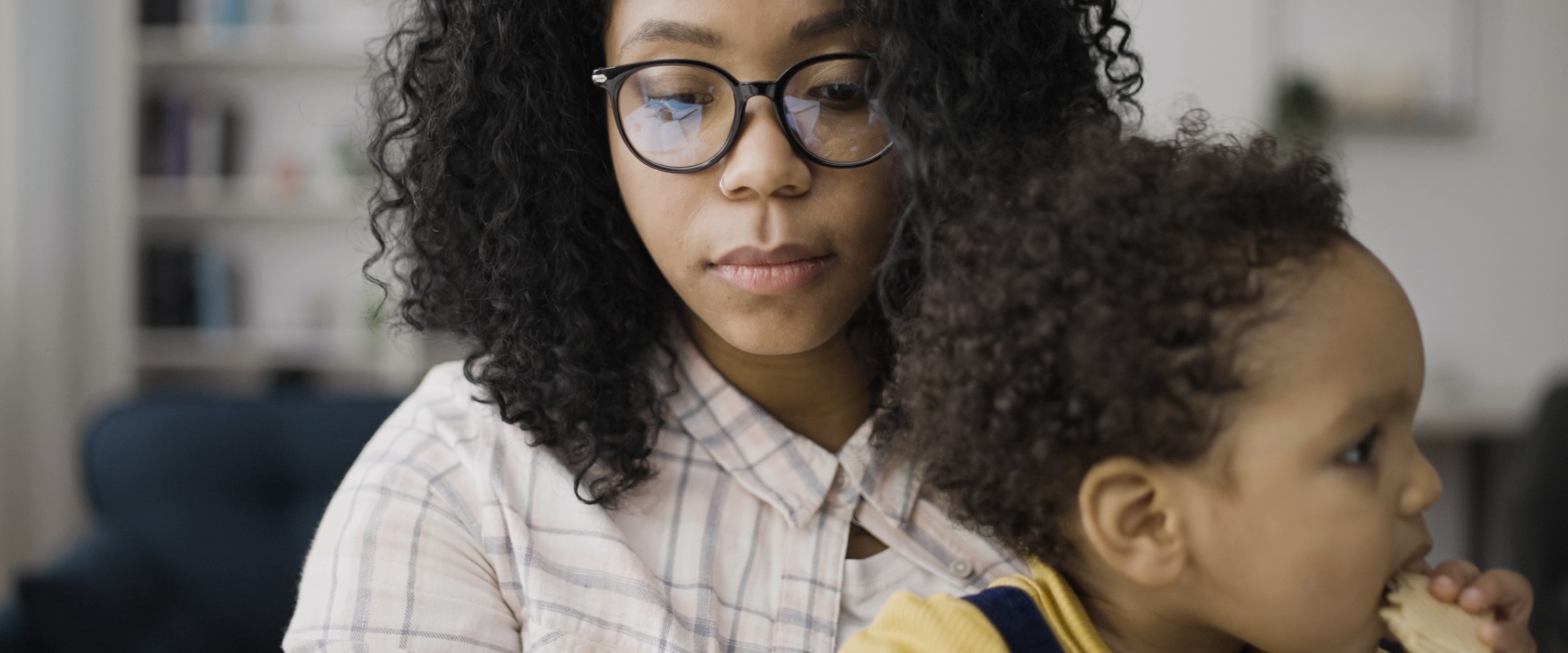 Photo of African American woman holding son as she works on computer.