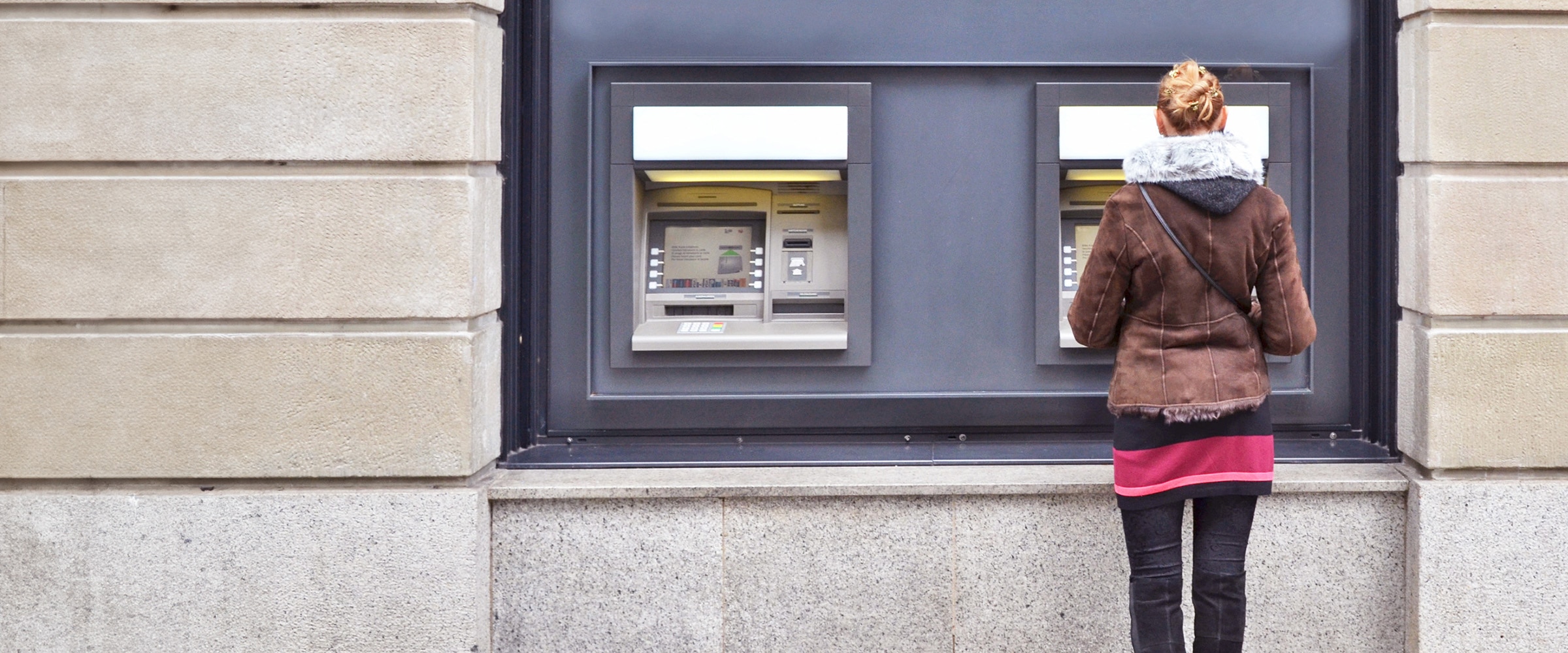 Photo of a woman standing in front of a bank's ATM machine.