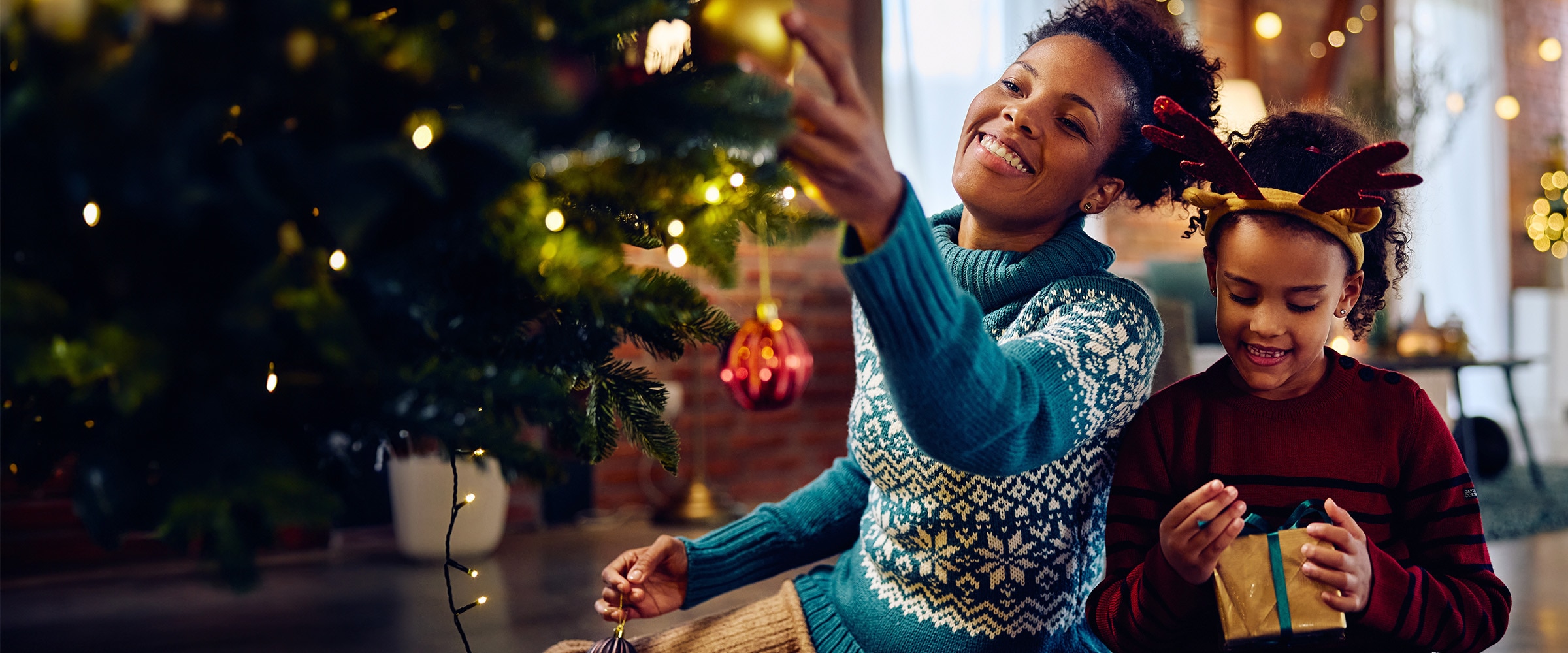 African-american mother and daugher kneel and hold presents around a holiday tree.