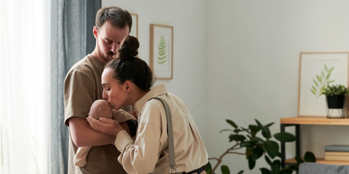 Photo of couple. Man is holding newborn and women is kissing newborn.