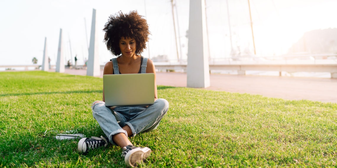 Photo of woman on grass working on her computer laptop.