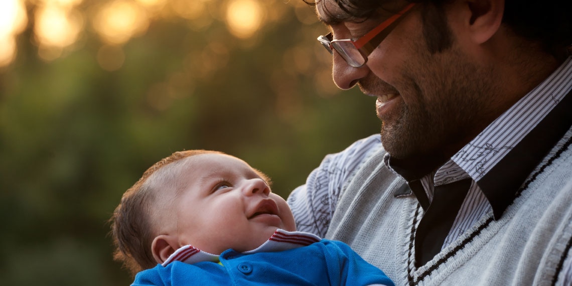 Photo of older man cradling baby in front of him.