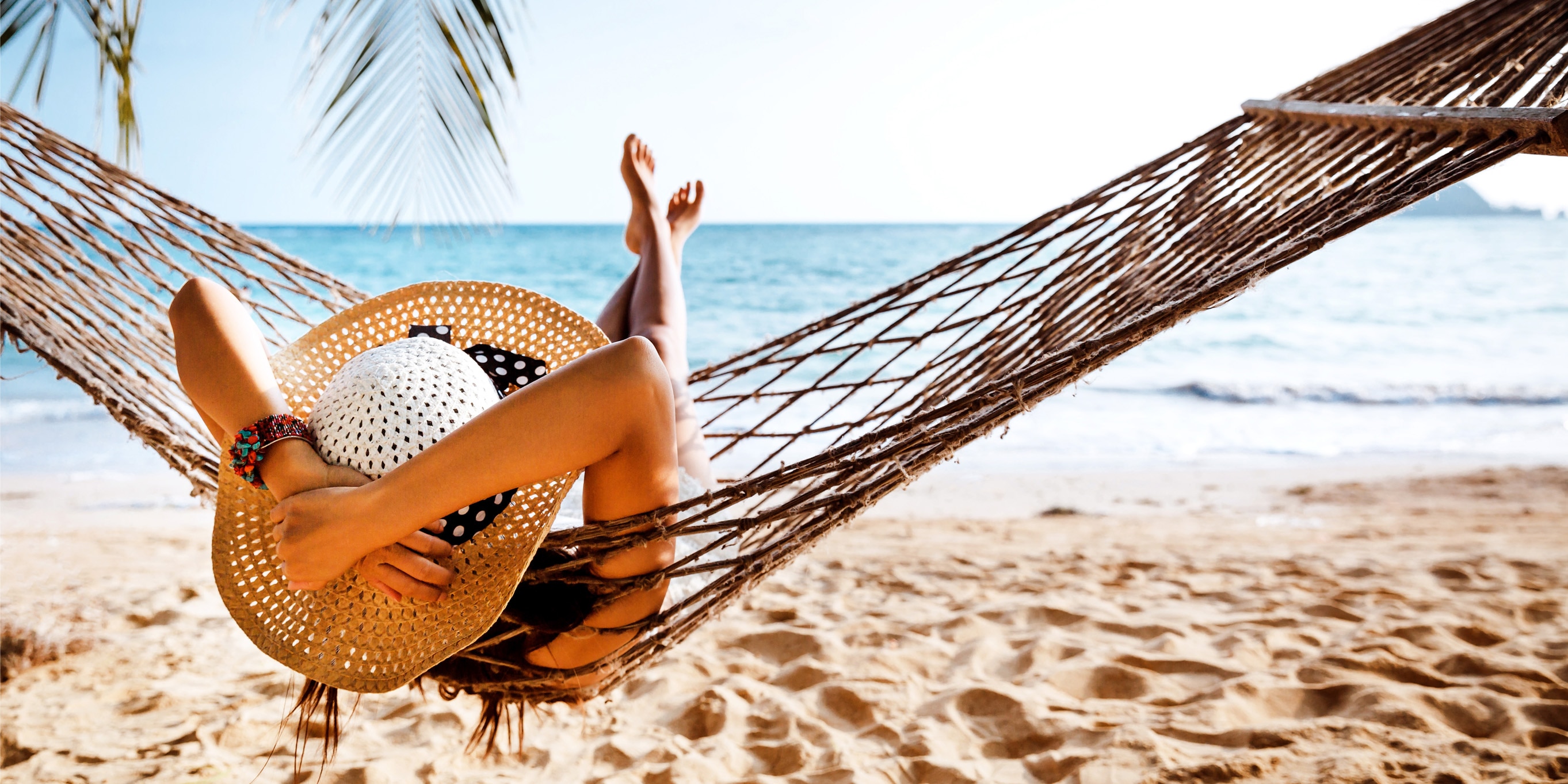 Photo of a woman with a large summer hat relaxing on hammock at the beach.