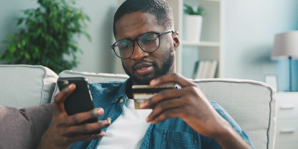 Photo of African American man looking at his credit card and phone in each hand.