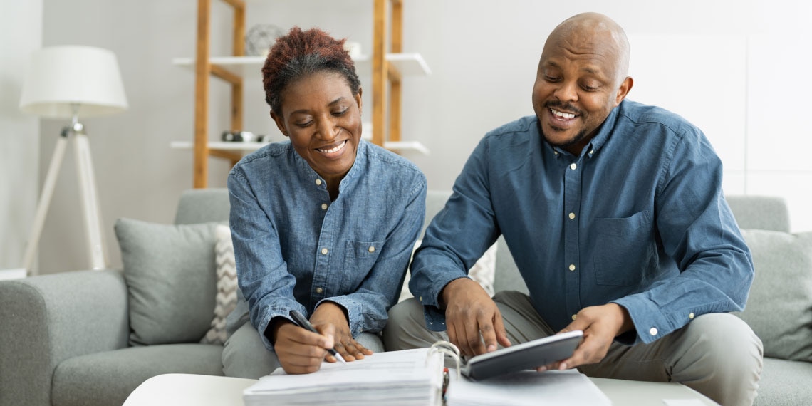 African-american couple sitting on couch looking at their finances.