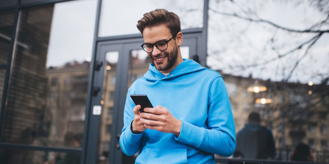 Photo of young man in blue hoodie looking at his smart phone.