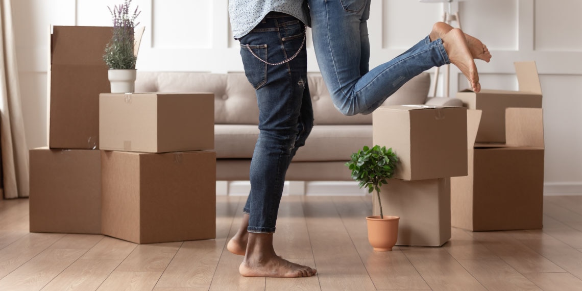 Photo of couple in embrace surrounded by moving boxes in new home.