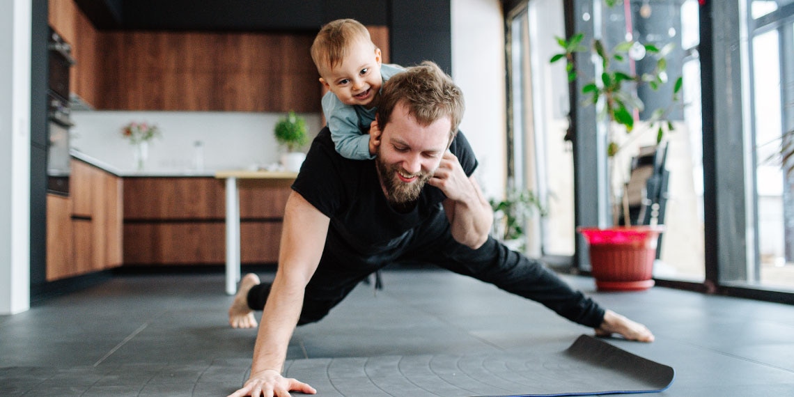 Photo of man doing one-armed pushup with a small child on his back.