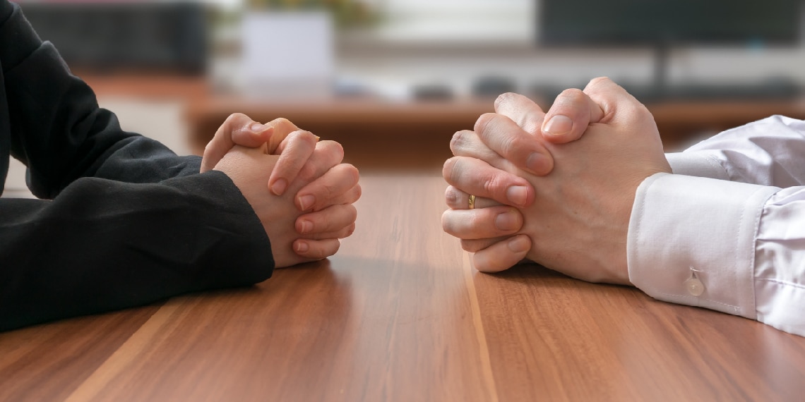 Photo of clasped hands facing each other across a work table.