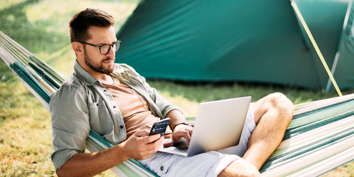 Photo of man looking at mobile phone while on a camping cot.