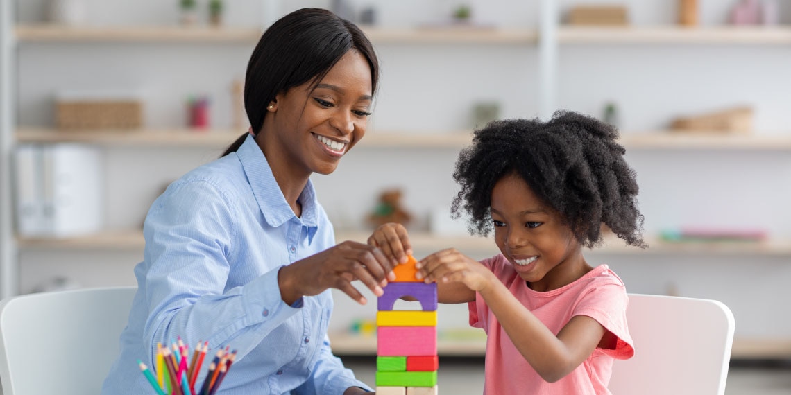 Photo of adult African American woman with child playing with colored toy blocks.