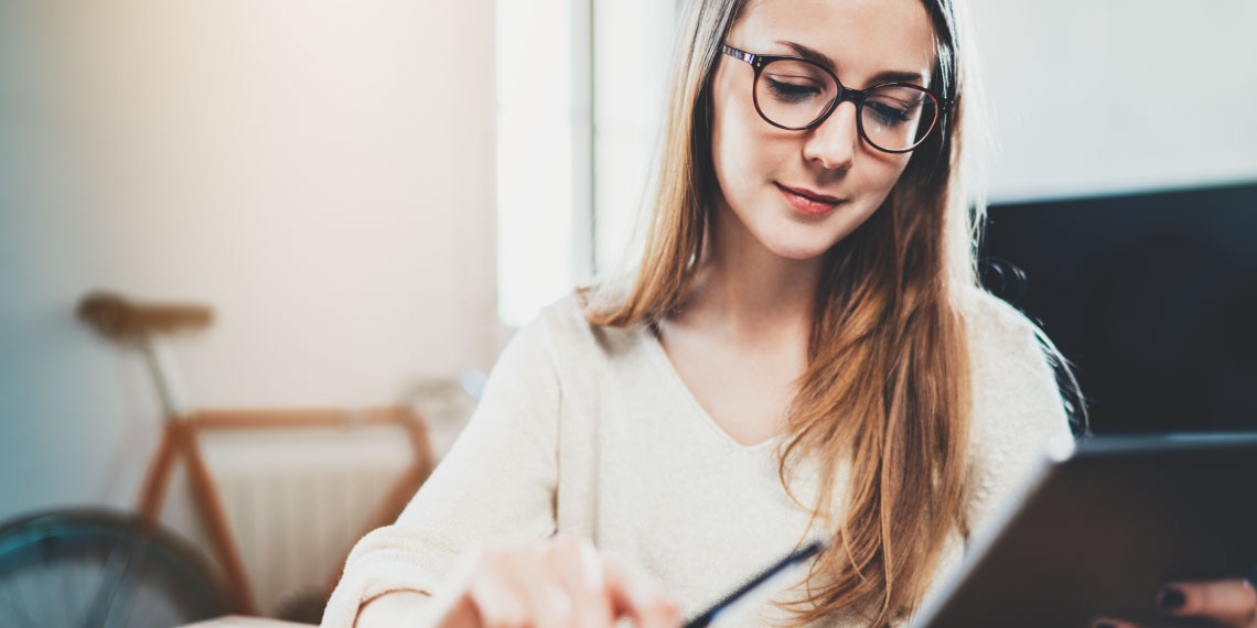 Photo of young woman in apartment looking at her electronic tablet.