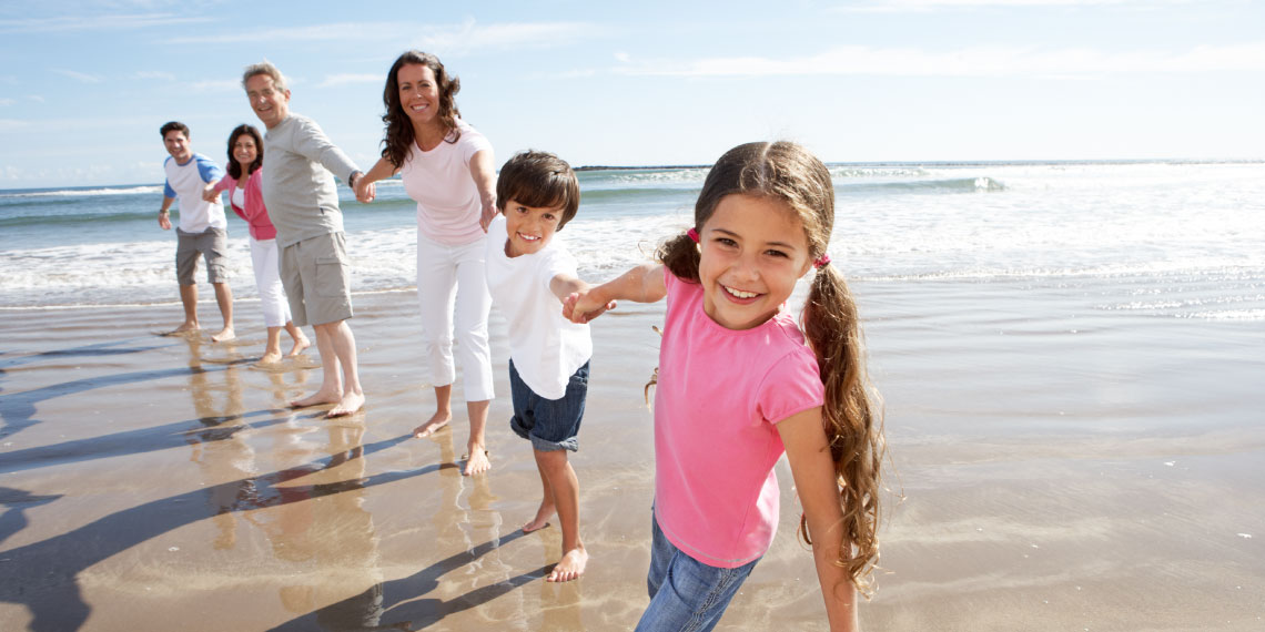 Photo of multi-generational family holding hands on the beach.